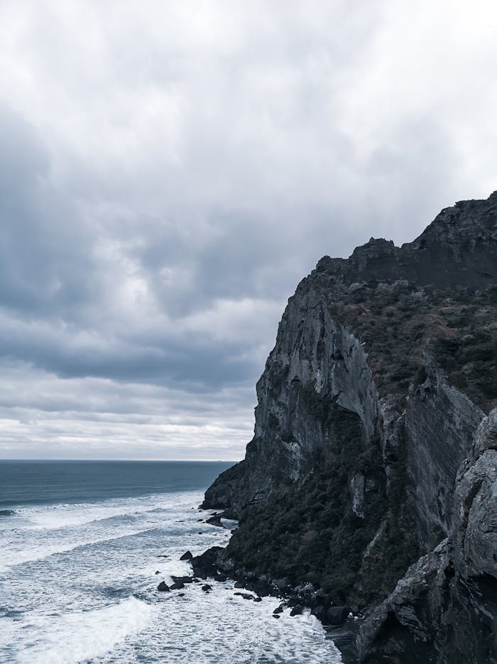 about-07 Experience the majestic cliffs and ocean waves under a moody gray sky, capturing nature's raw beauty.