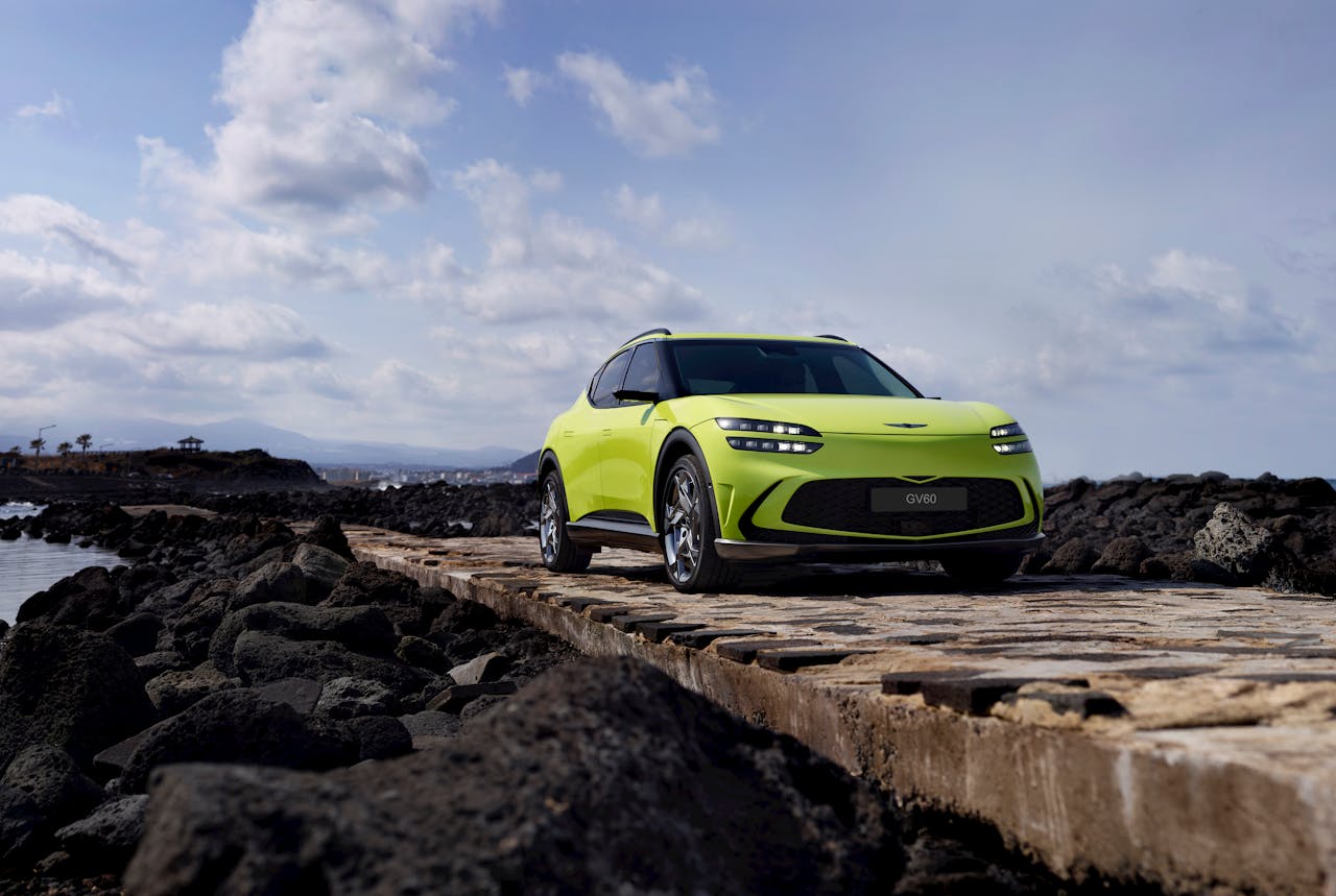 A vibrant green car parked on a rocky path along the scenic Jeju coastline under a partly cloudy sky.