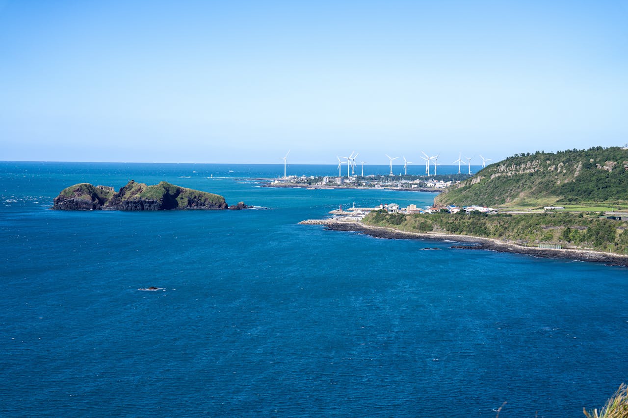 Scenic view of Jeju Island coastline with wind turbines under clear blue skies.