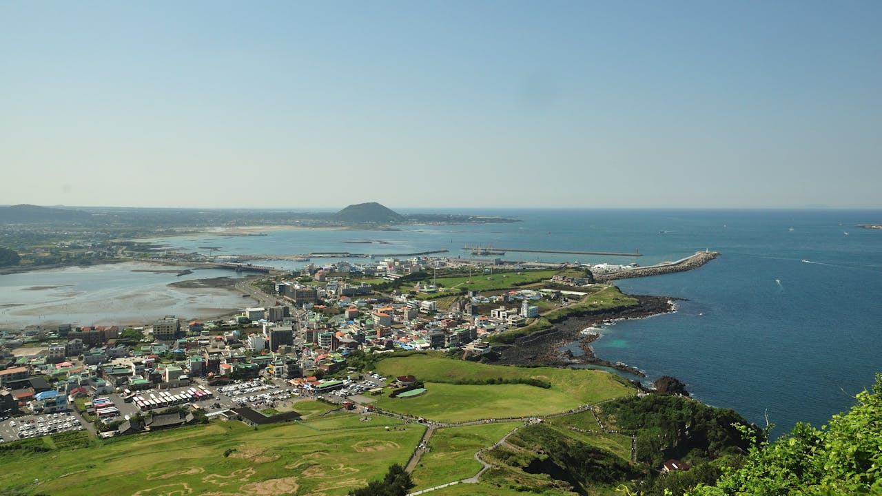 about-01 A breathtaking aerial view of Jeju Island's coastline, showcasing the vibrant city and blue ocean.